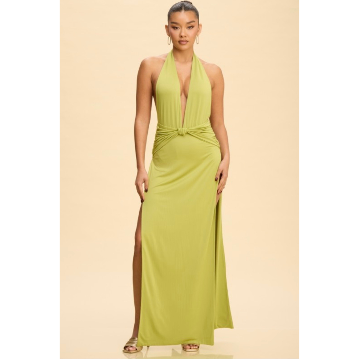 A woman modeling a lime green halter-neck maxi dress with a plunging V-neckline, a twisted waist detail, and a high side slit, set against a solid beige background.