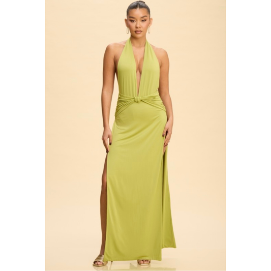 A woman modeling a lime green halter-neck maxi dress with a plunging V-neckline, a twisted waist detail, and a high side slit, set against a solid beige background.